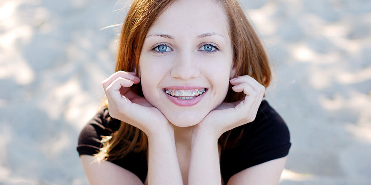 Young lady with braces smiling and holding her face in both hands