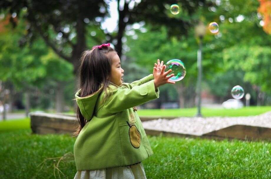 Young girl playing in a park getting ready to burst a bubble.