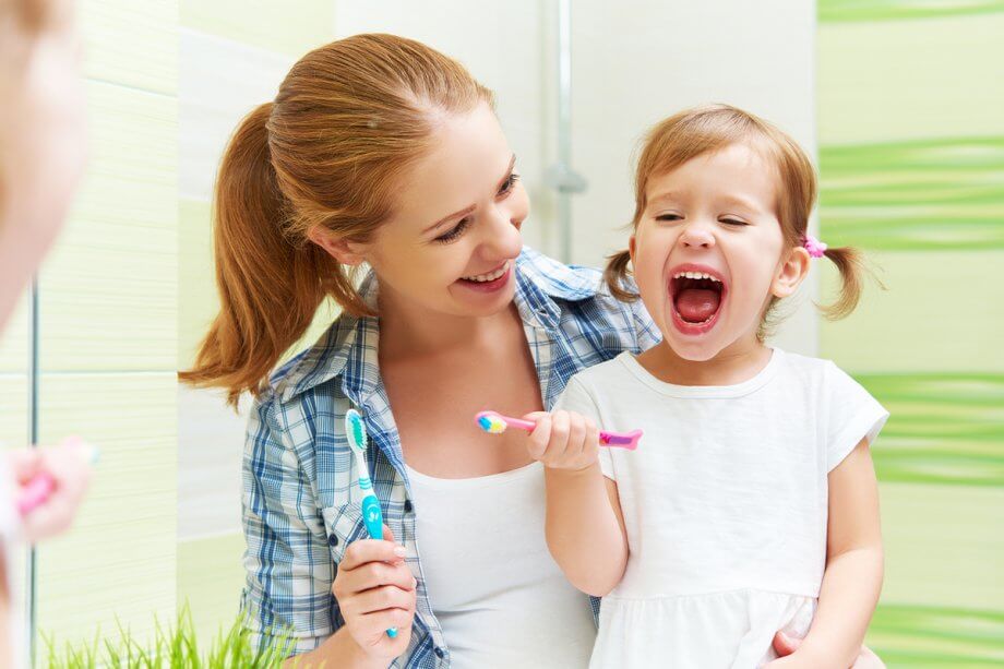 mom and young daughter brush teeth