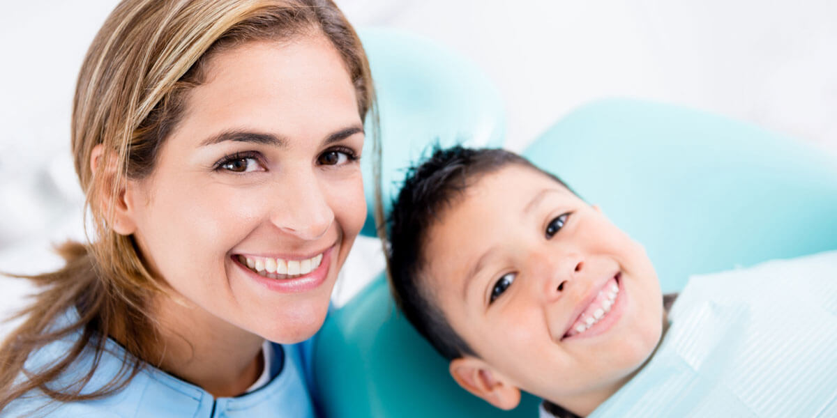Smiling dental assistant and young boy smiling in dental chair